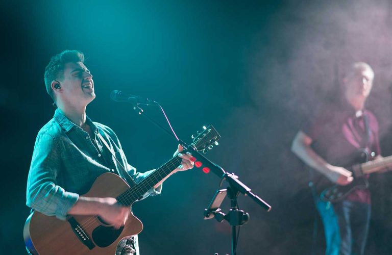 A guitarist plays acoustic folk guitar on stage